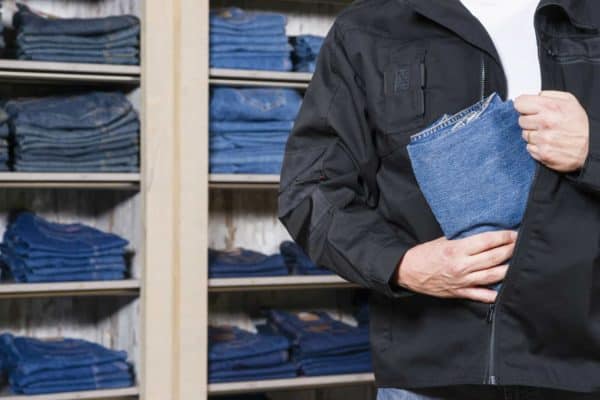 A man puts jeans in his jacket to illustrate organized retail theft laws in California