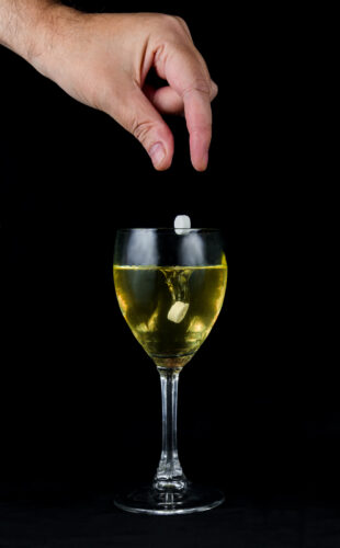A hand dropping pills in a drink to perform a date rape