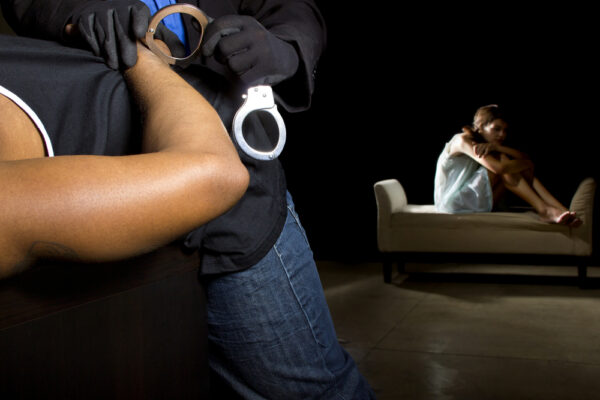 A man is handcuffed while a potential rape victim looks depressed on the bed