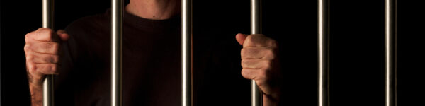 A man's hands behind prison bars