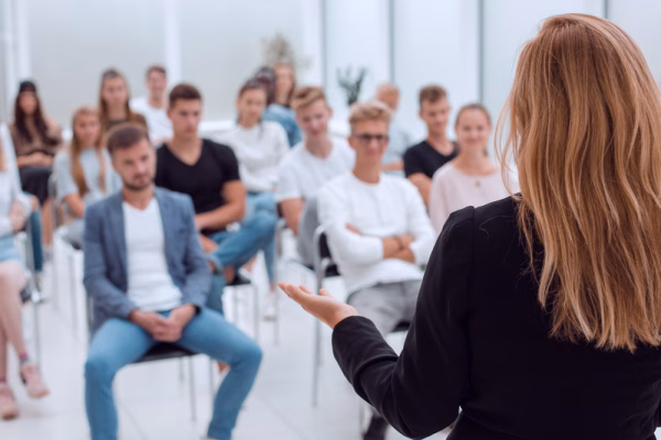 A woman speaking in front of a group of seated individuals that could be participating at a DUI class in California or a MADD VIP program.